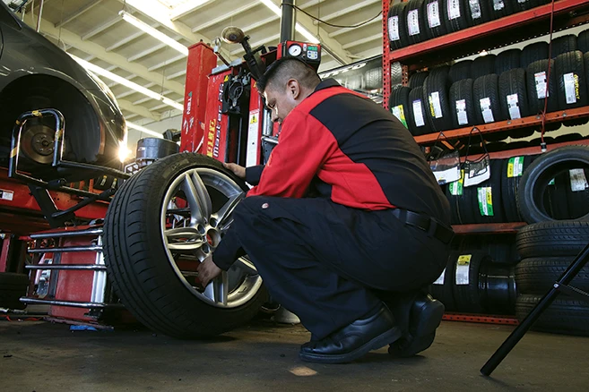 Automotive Uniform Rentals - Auto technician in branded uniform putting on new tires