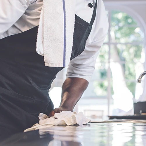 Restaurant Uniform Rentals from Oregon Linen - Kitchen Staff Wiping Down Stainless Steel Counter with White Towel