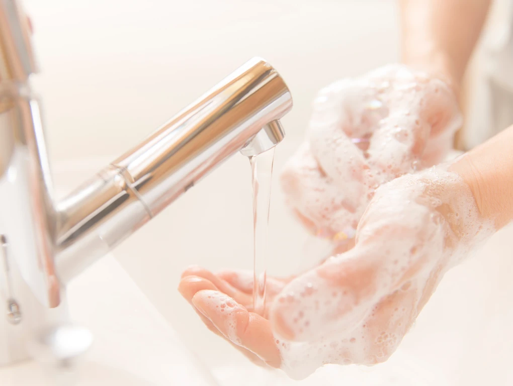Person washing hands under running water, soapy hands
