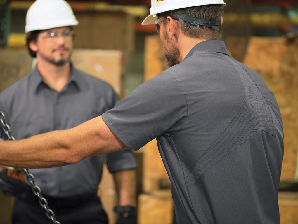 Two men wearing industrial uniforms and hard hats on a job site
