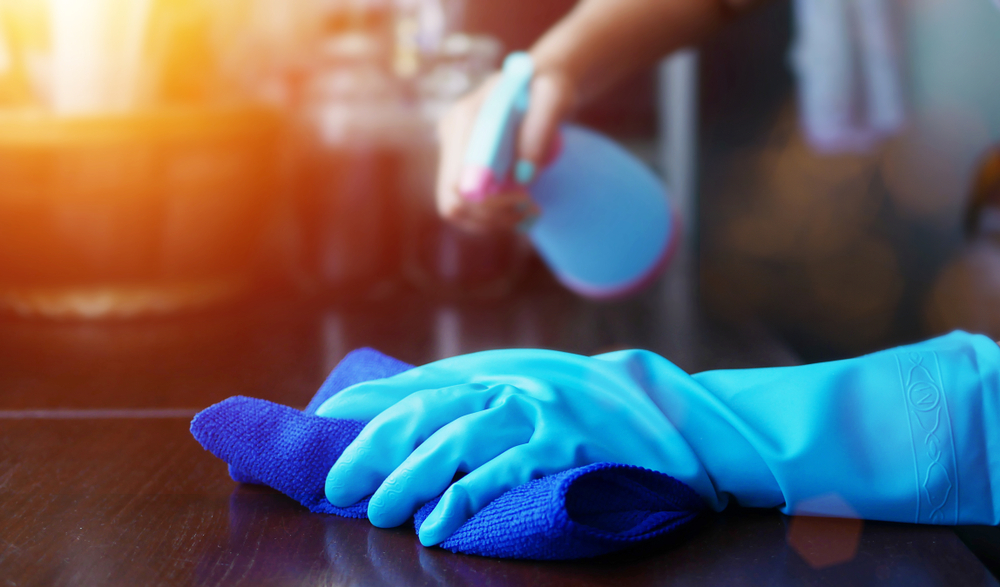 microfiber-towel-benefits Cleaner wiping down table with disinfectant spray and blue microfiber towel